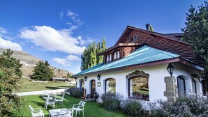 A rustic wooden house with a green roof, surrounded by a well-maintained lawn and white chairs.