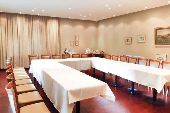 A conference room with long tables and chairs, beige curtains, framed pictures on the walls, and a painting.
