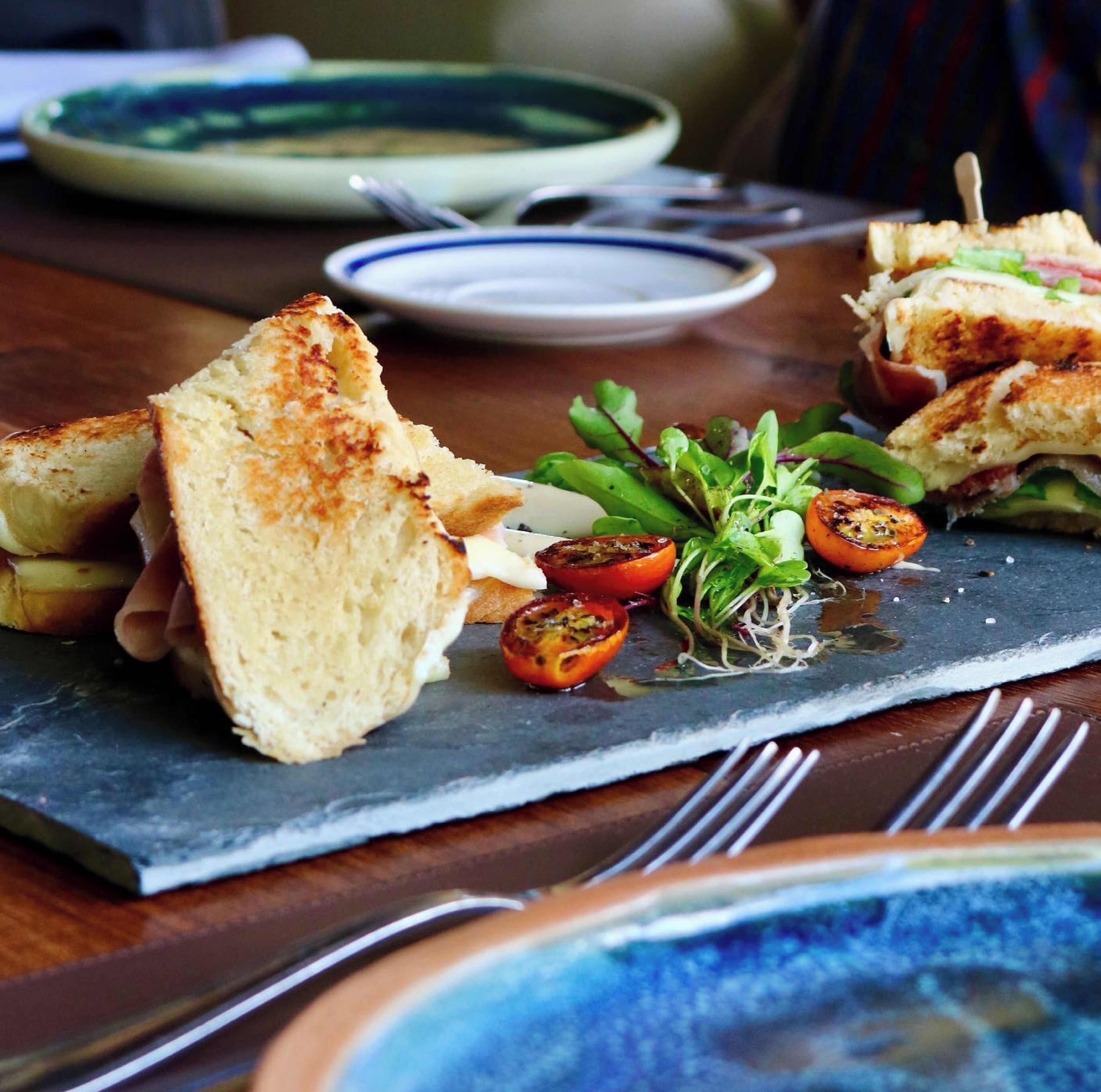 A meal consisting of grilled sandwiches and a side salad with tomatoes and greens on a slate board.
