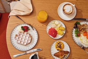 Una mesa de desayuno con waffles, fruta, cruasanes, café y jugo.