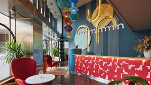 A modern hotel lobby with a reception desk, red and blue chairs, and decorative lighting. - Hotel Indigo Barcelona Plaza Espana by IHG (Barcelona)