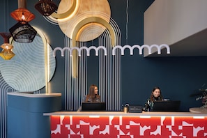 Un mostrador de recepción con dos empleados, luminarias modernas y una pared decorativa con un diseño de la letra 'm'.