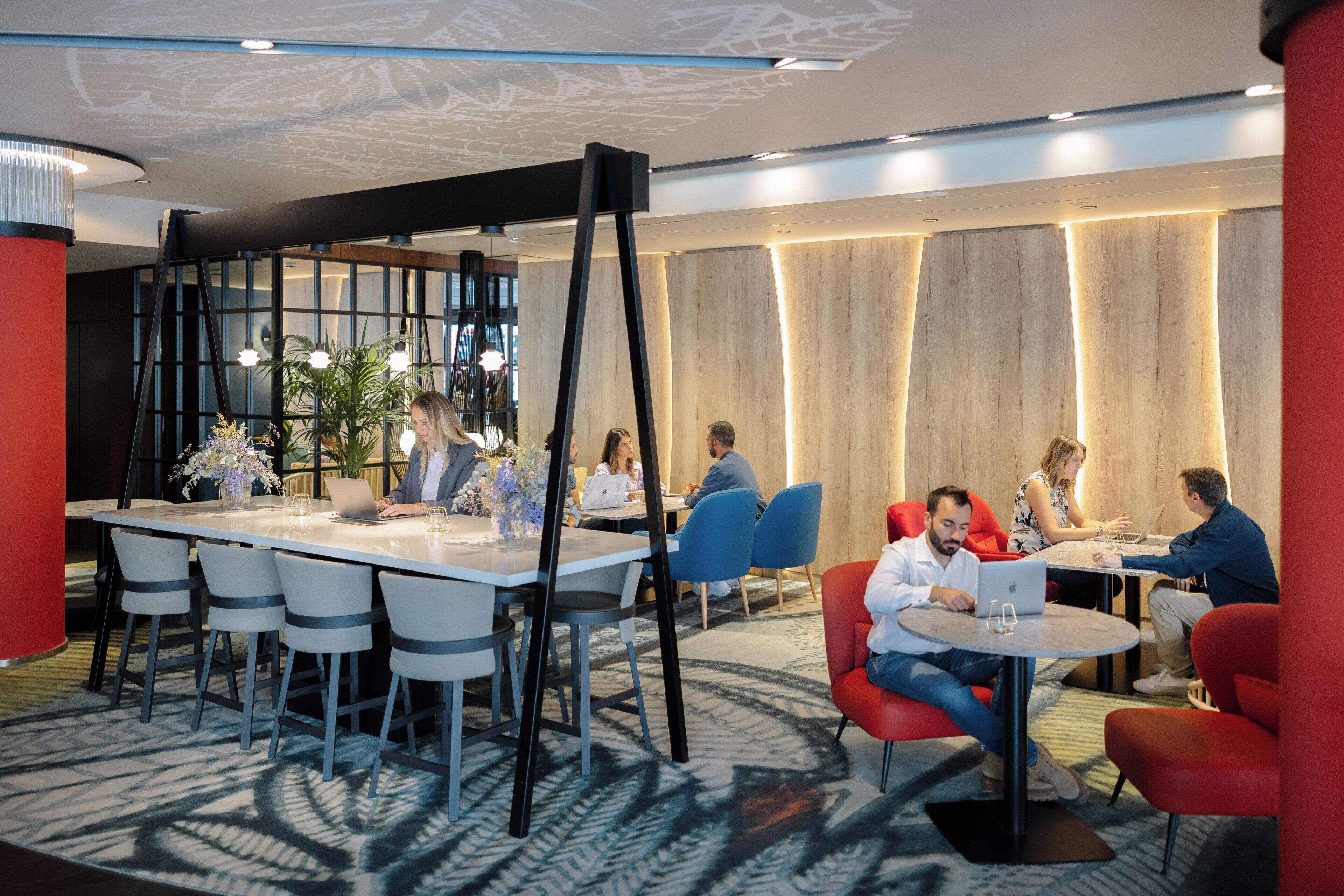 A modern conference room with a long table, several chairs, and round tables with laptops.