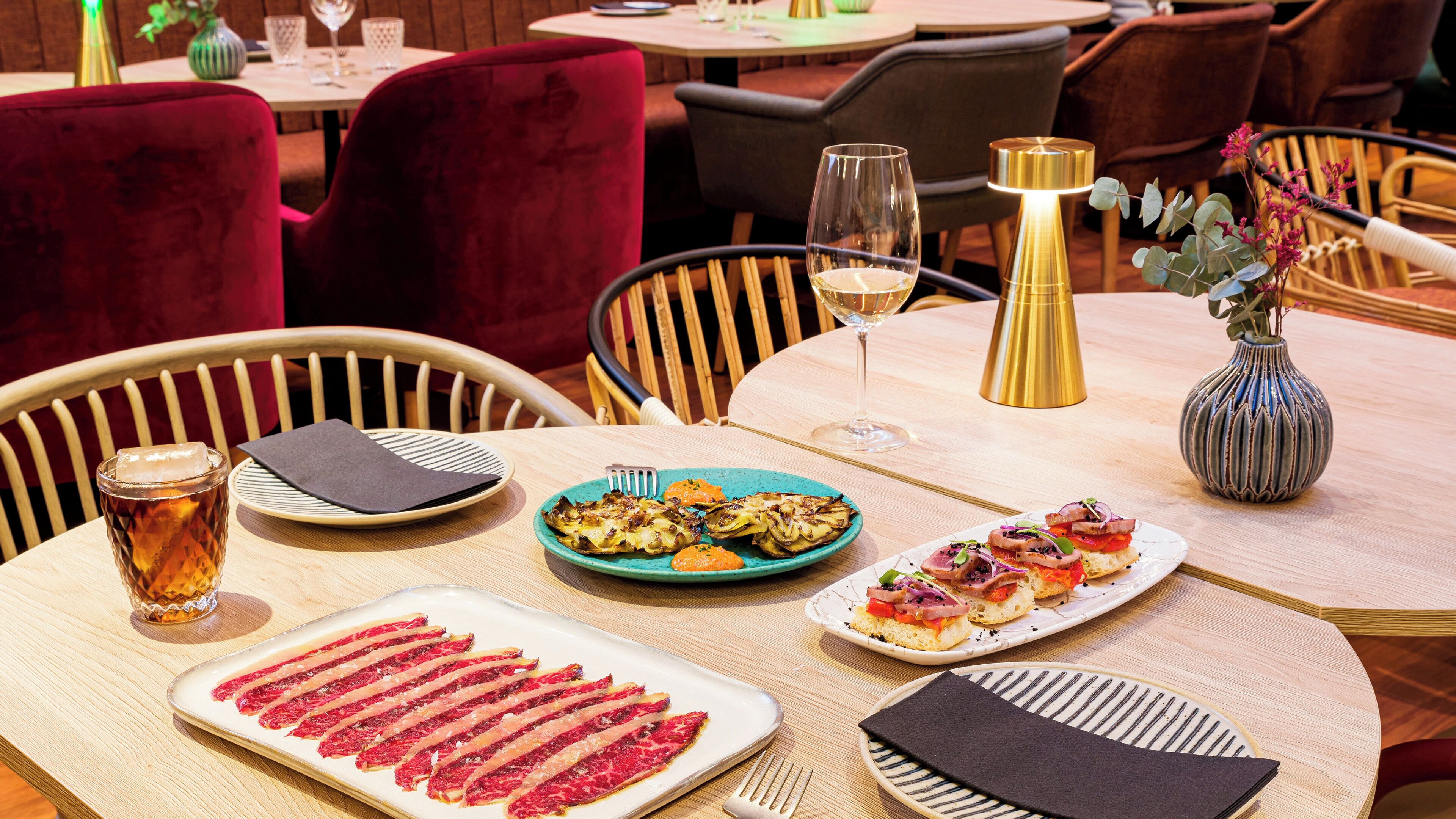 Een restauranttafel, gedekt voor een maaltijd, met borden eten, een glas wijn en een vaas bloemen.