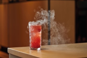 Una bebida roja en un vaso, con vapor elevándose, sobre una superficie de madera.