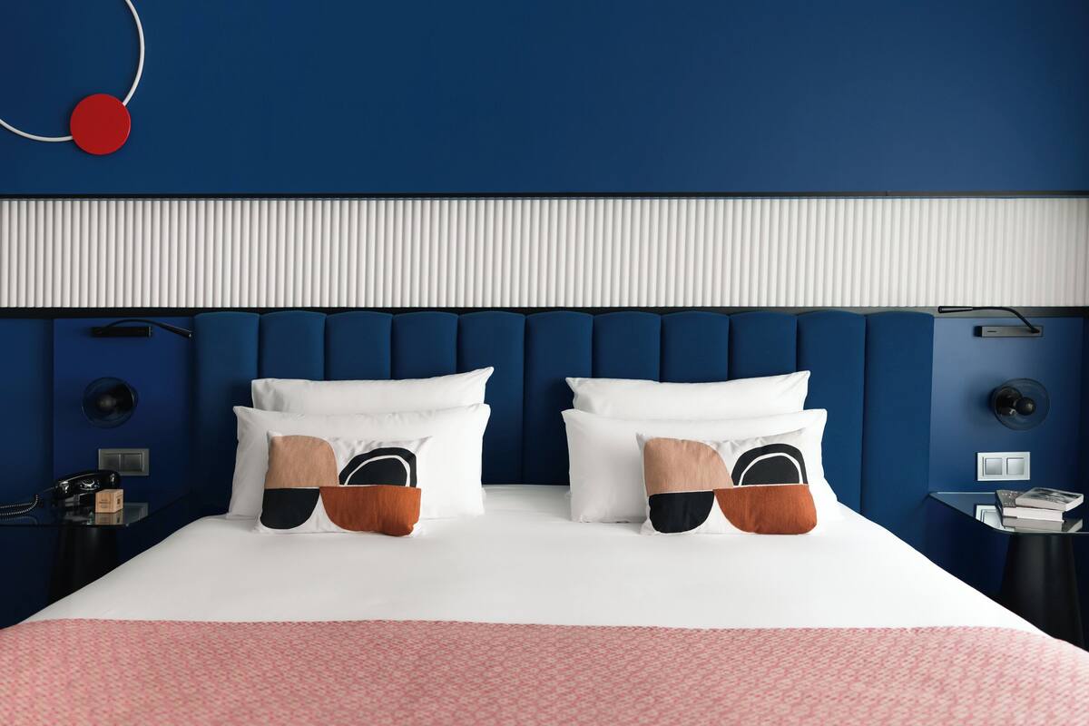Una habitación de hotel moderna con una cama grande, una mesita de noche y un objeto circular rojo en la pared.