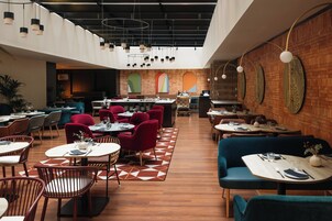 A modern restaurant with round tables, red and blue upholstered chairs, and a geometric patterned floor.
