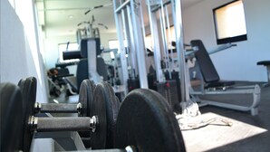 A gym with exercise equipment, a treadmill, and a television on the wall. - Hotel Campestre Inn (León)