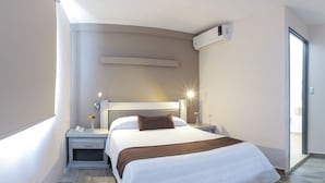 A modern hotel room with a large bed, bedside tables, a nightstand, a wall-mounted air conditioner, and a sliding glass door to the balcony. - Hotel Campestre Inn (León)