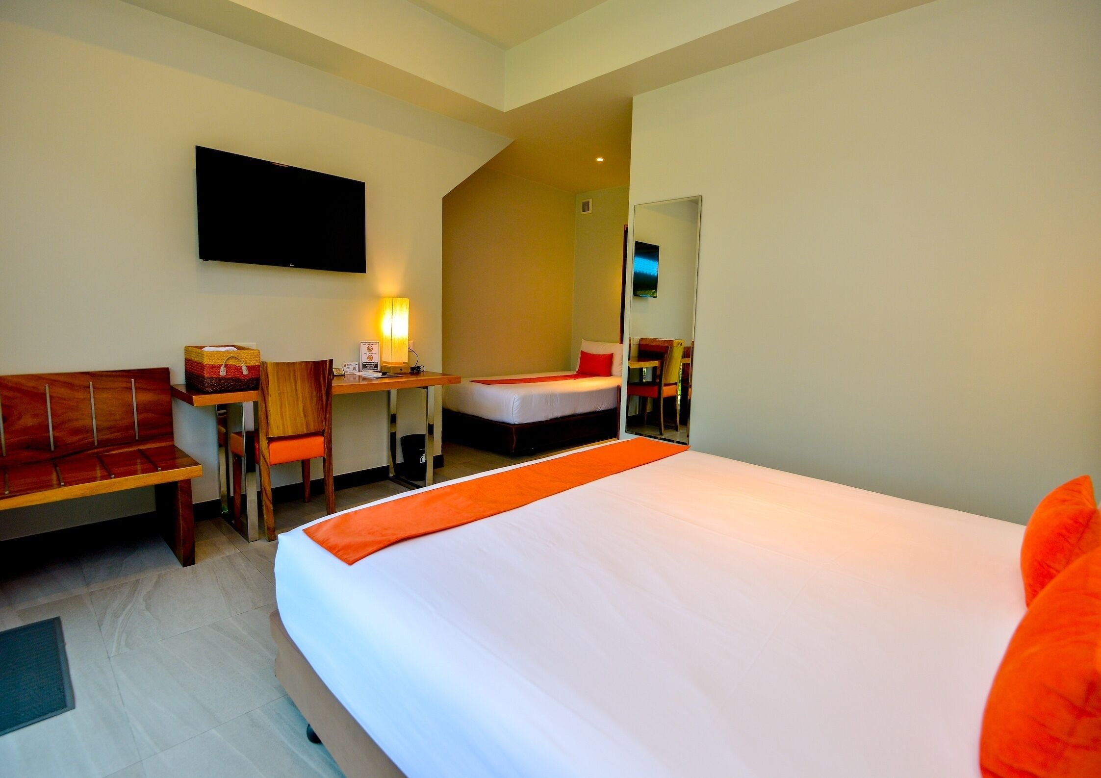 A hotel room with a large bed, a desk, a chair, a sofa, and a flat-screen TV on the wall.