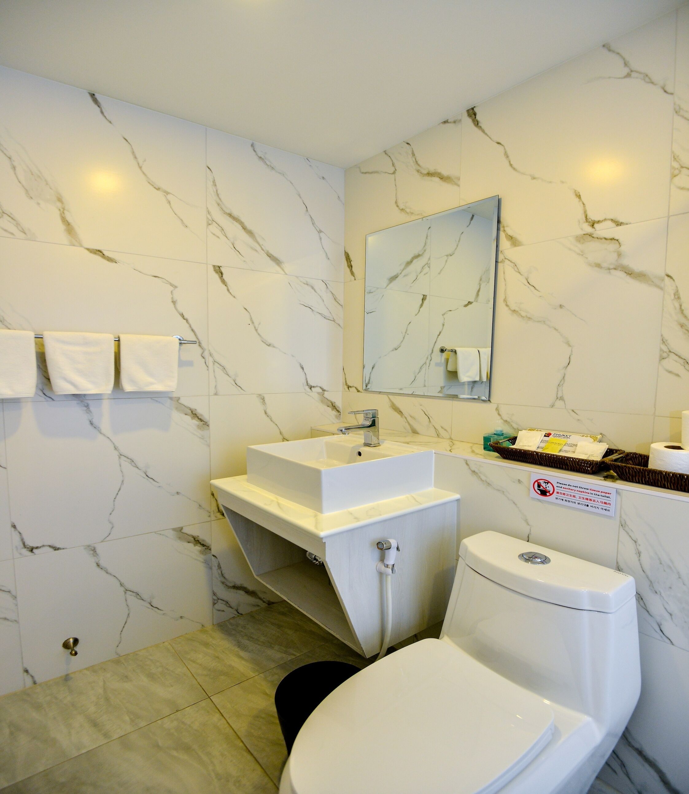A bathroom with a marble wall, a sink, a toilet, and a mirror.