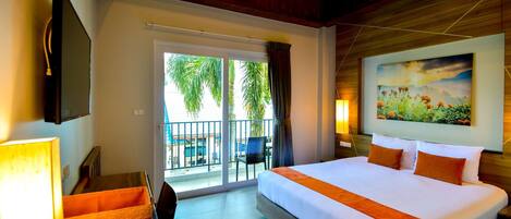 A hotel room with a large bed, a TV, a balcony with a view of palm trees, and a painting on the wall.