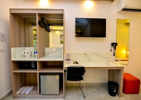 Habitación de hotel compacta con kitchenette, televisión, espejo y un pequeño rincón de descanso.