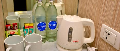 Una kitchenette con un hervidor eléctrico blanco, dos botellas de agua Crystal, varios pods de café Nescafé y dos tazas blancas sobre una encimera de mármol.