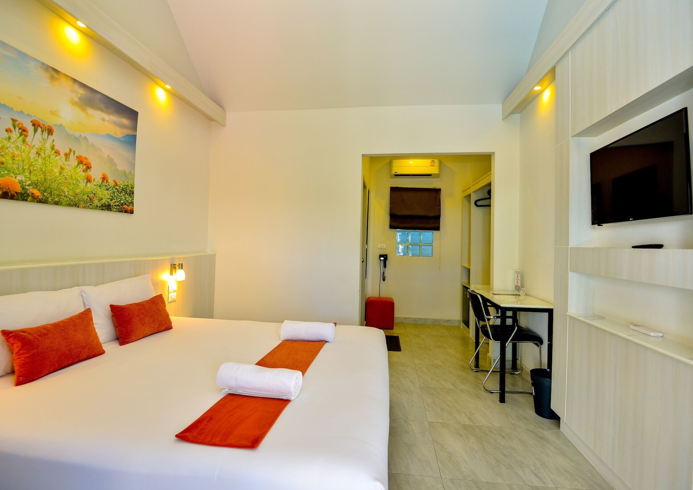 A hotel room with a large bed, a desk, a TV, and a painting on the wall.