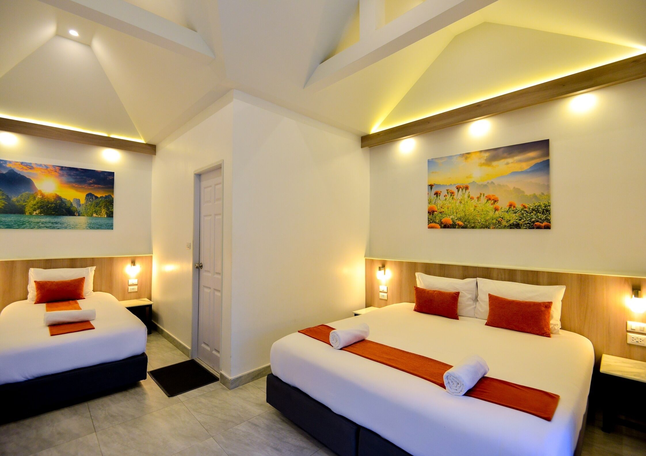 A hotel room with two beds, each with white linens and orange accents, a wooden headboard, and a painting of a sunset on the wall.