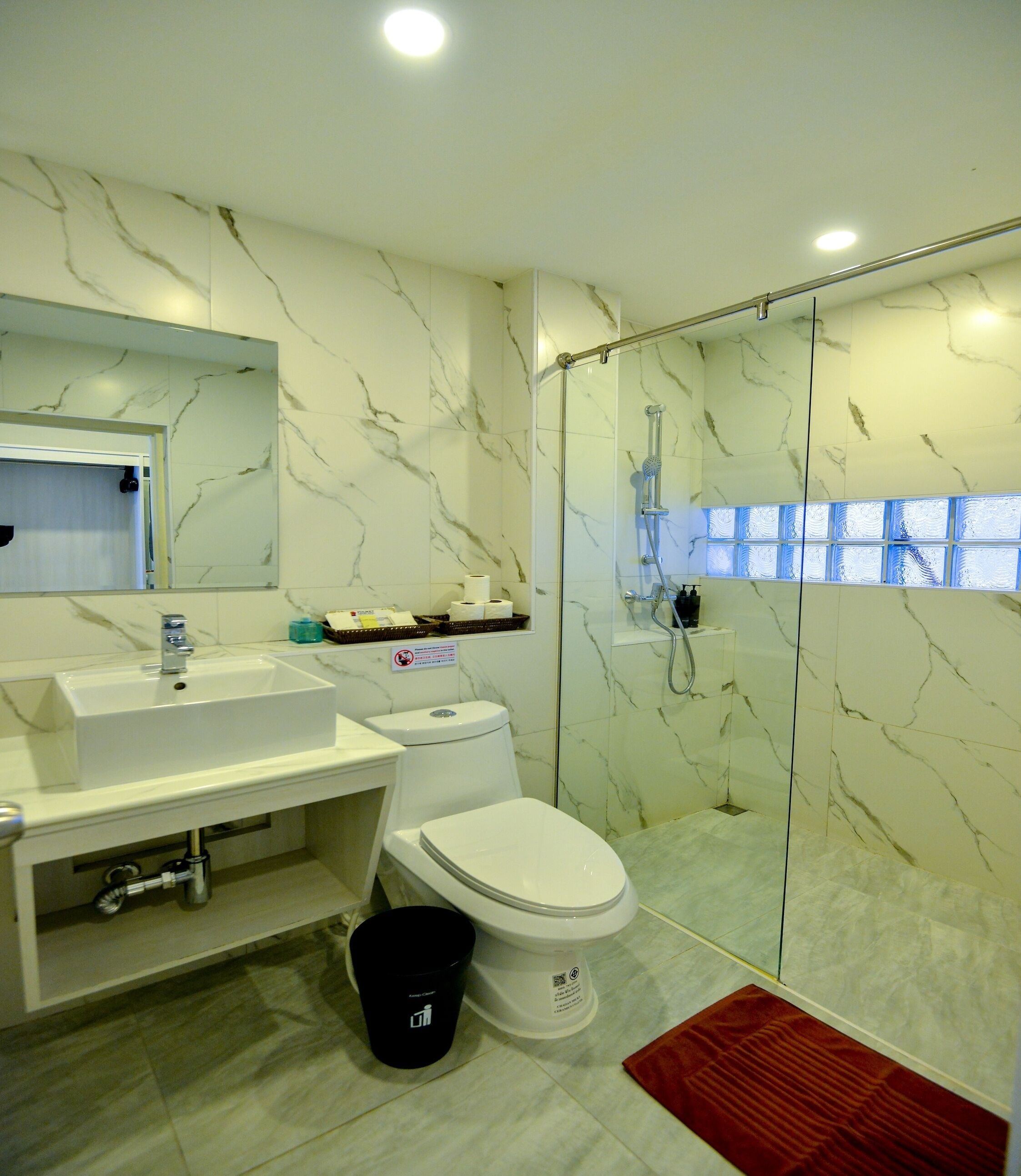 Un baño moderno con salpicadero de mármol, ducha con mampara de vidrio, lavabo blanco y un inodoro.