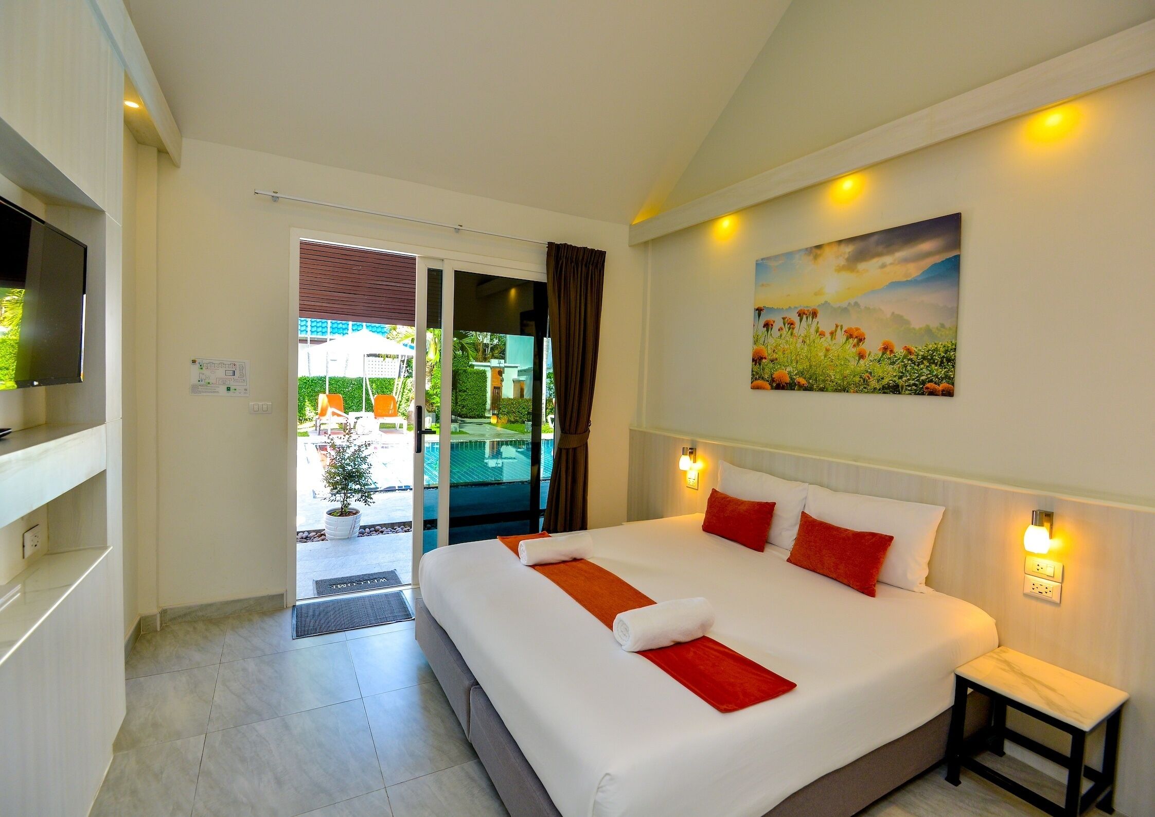 A hotel room with a bed, a TV, a painting, and a view of an outdoor pool.
