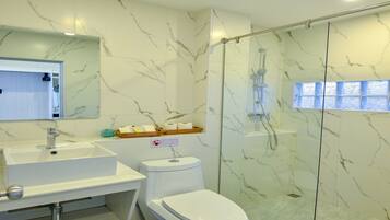 Un baño moderno con detalles de mármol, cabina de ducha con mampara de vidrio, lavamanos blanco y un inodoro.