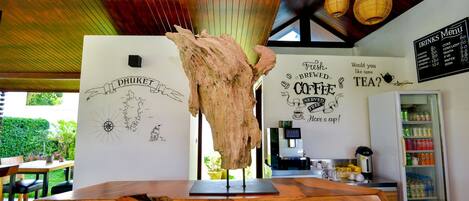 Una mesa de madera con un diseño único, una pared con un mapa y texto relacionado con el café, una pizarra de menú y un dispensador de bebidas.
