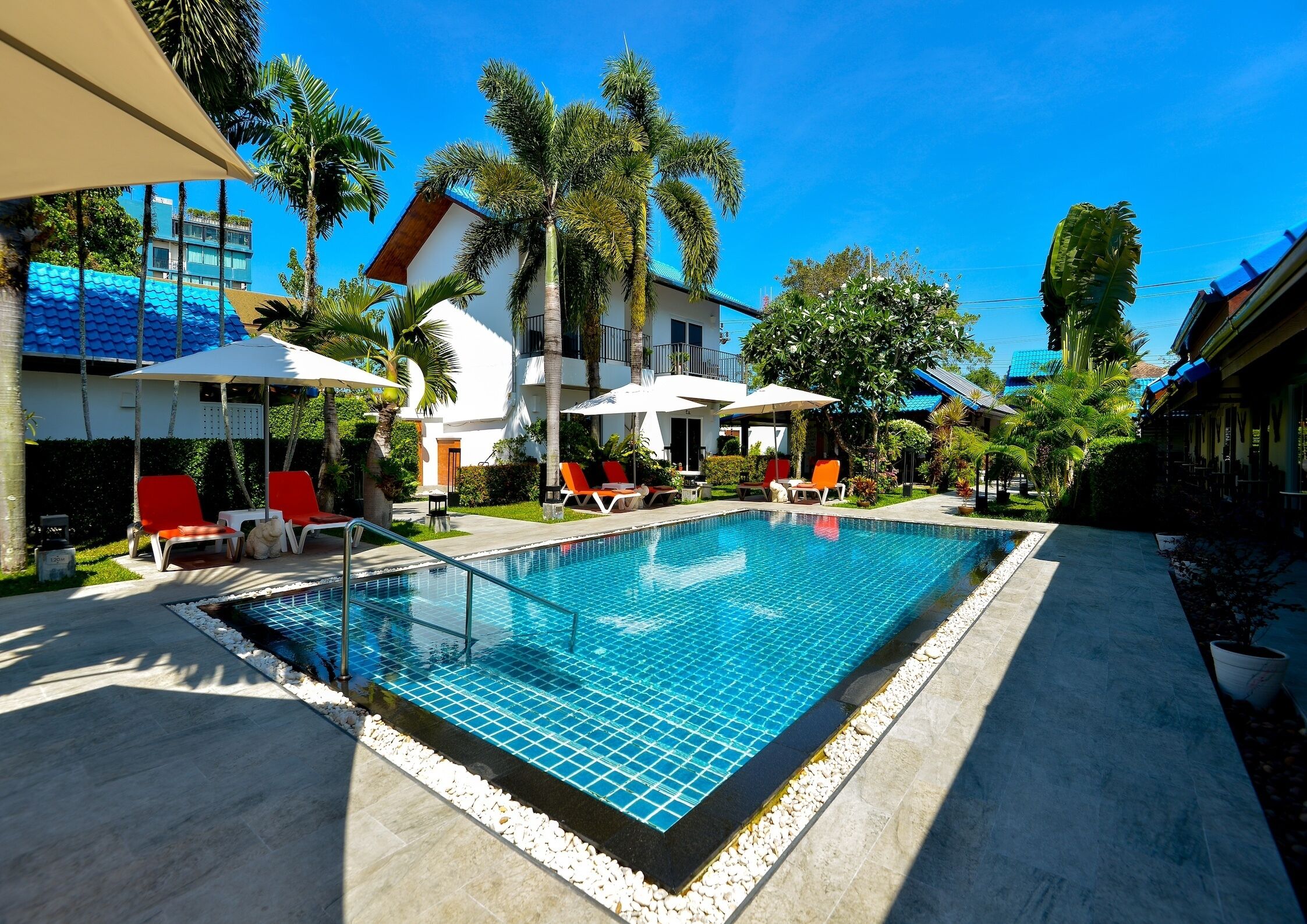 Una piscina con lettini, palme e un edificio con tetto blu.