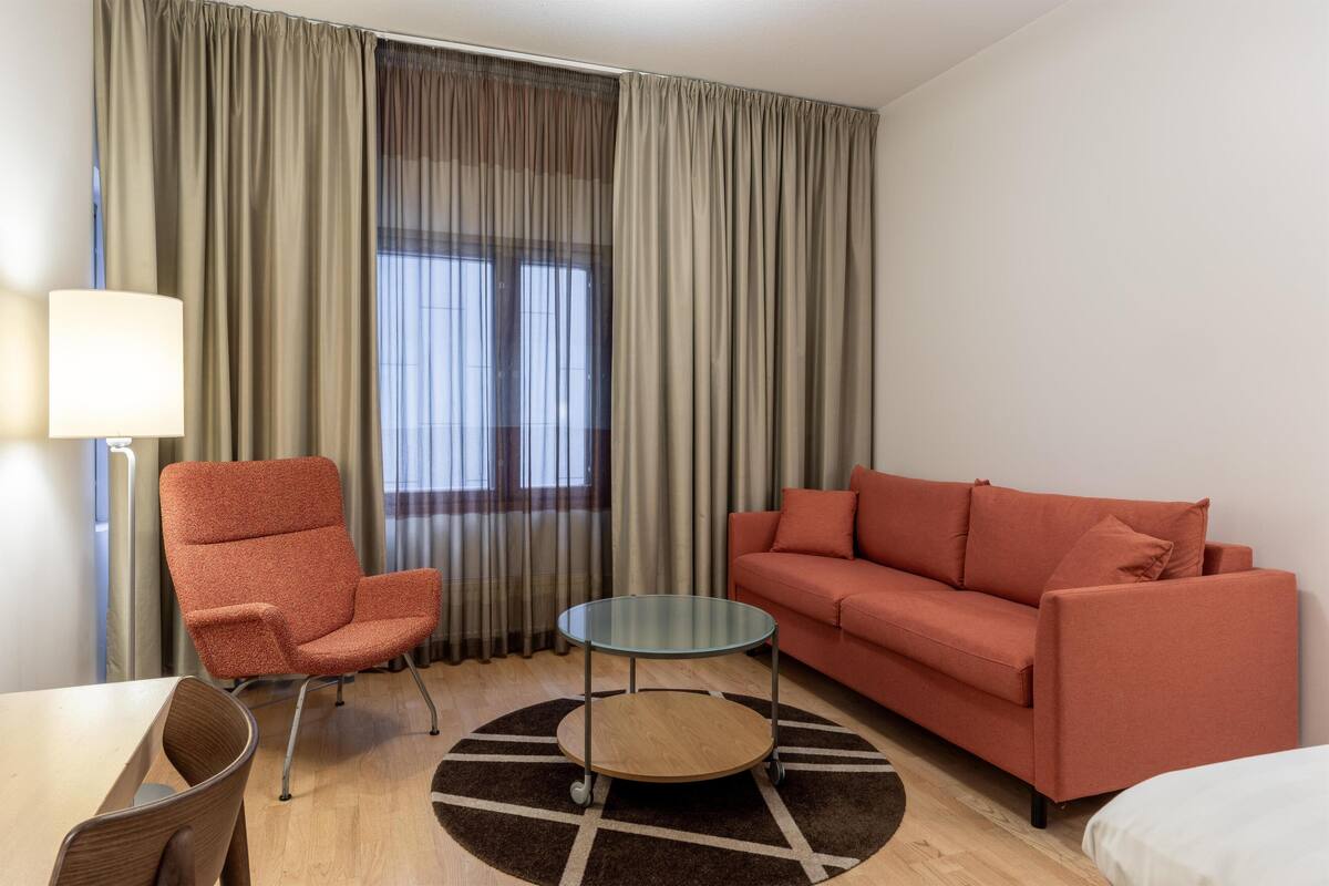 Habitación de hotel con sofá, sillón, mesita redonda y una lámpara.
