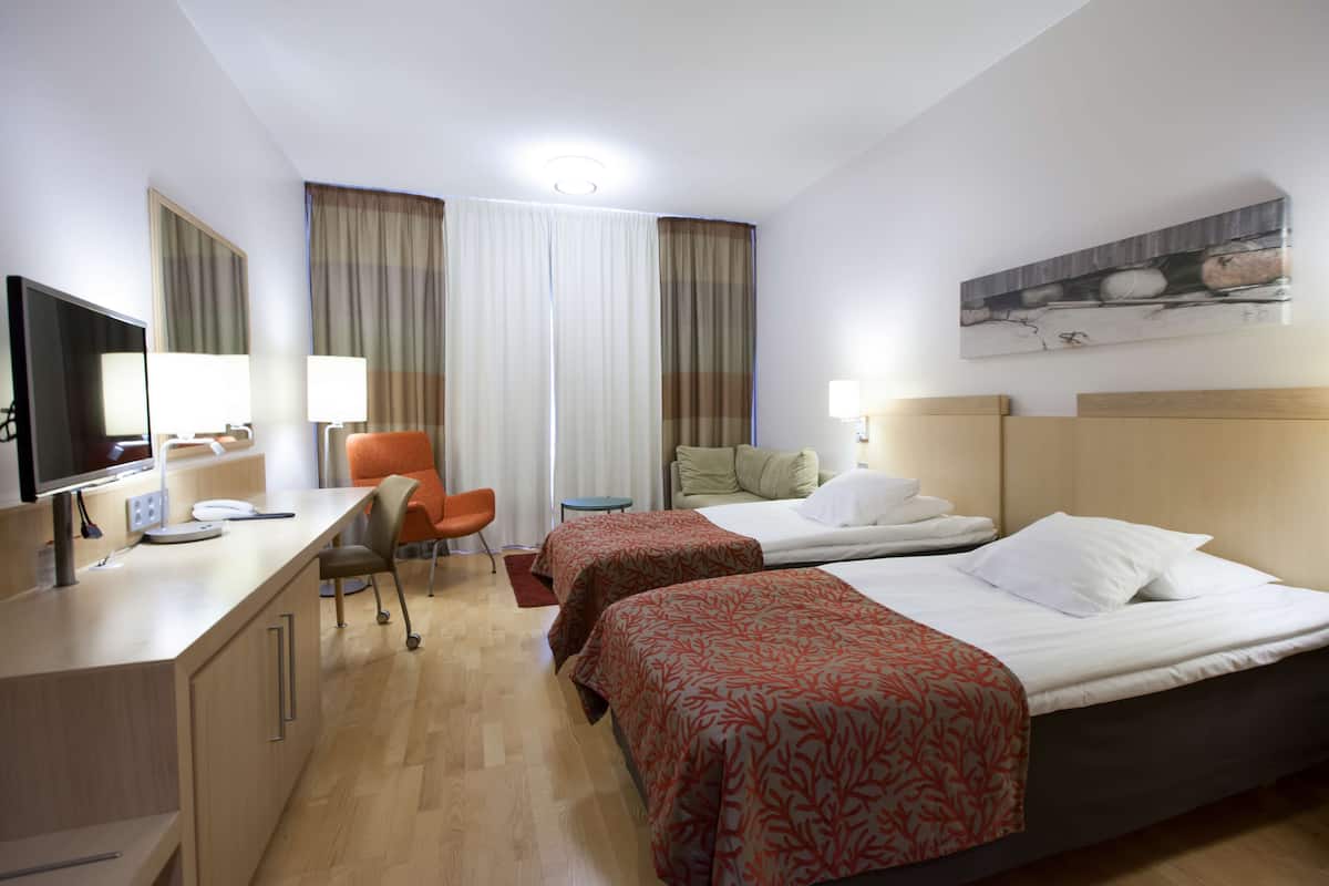 Habitación de hotel con dos camas, un escritorio con computadora, una silla y un televisor.