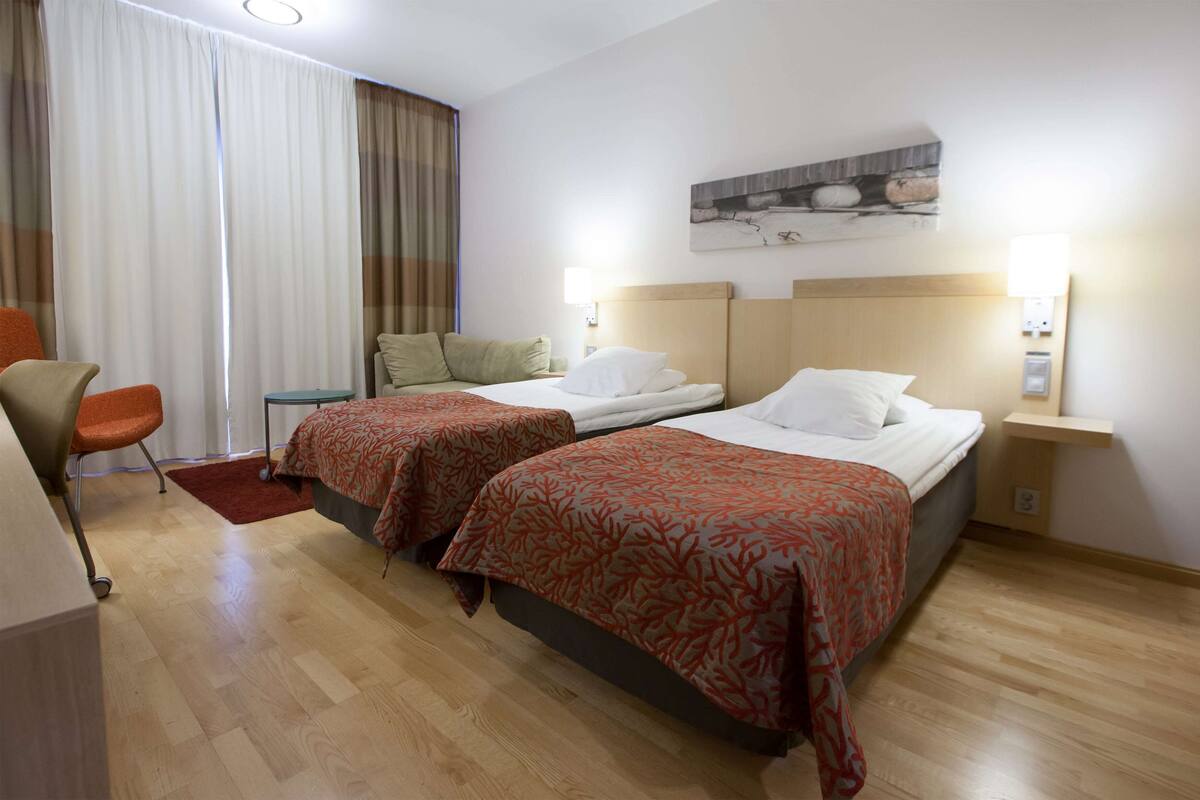 Habitación de hotel con dos camas, un escritorio, una silla y un ventanal con cortinas.