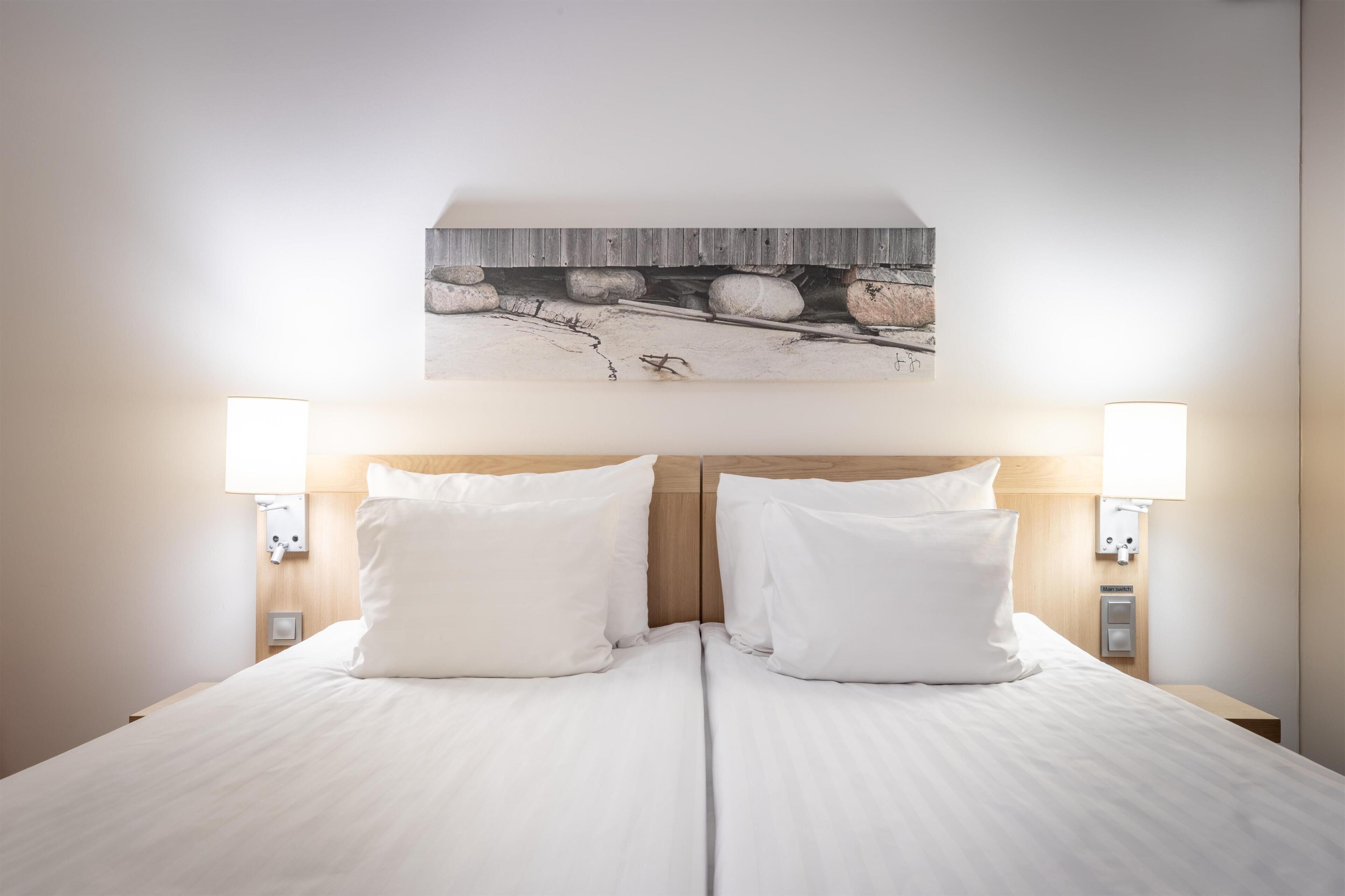 A double bed with white linens, two bedside lamps, and a wall-mounted artwork above.