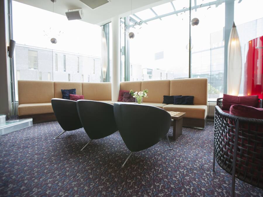 Un'area lounge moderna con un divano, due poltrone nere, un tavolino e una poltrona in vimini. Ampie finestre offrono vista sulla città.