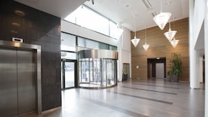 Un vestíbulo moderno con una puerta giratoria, un mostrador de recepción y una planta grande en maceta.