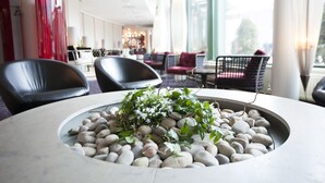 Un interior moderno con una mesa redonda rodeada de piedras y plantas, sillas de cuero negro y vistas de la ciudad a través de amplios ventanales.