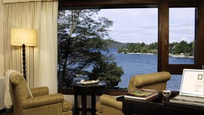 A room with two armchairs, a small table with a laptop, a lamp, and a view of a lake and forest. - El Casco Art Hotel (San Carlos de Bariloche)