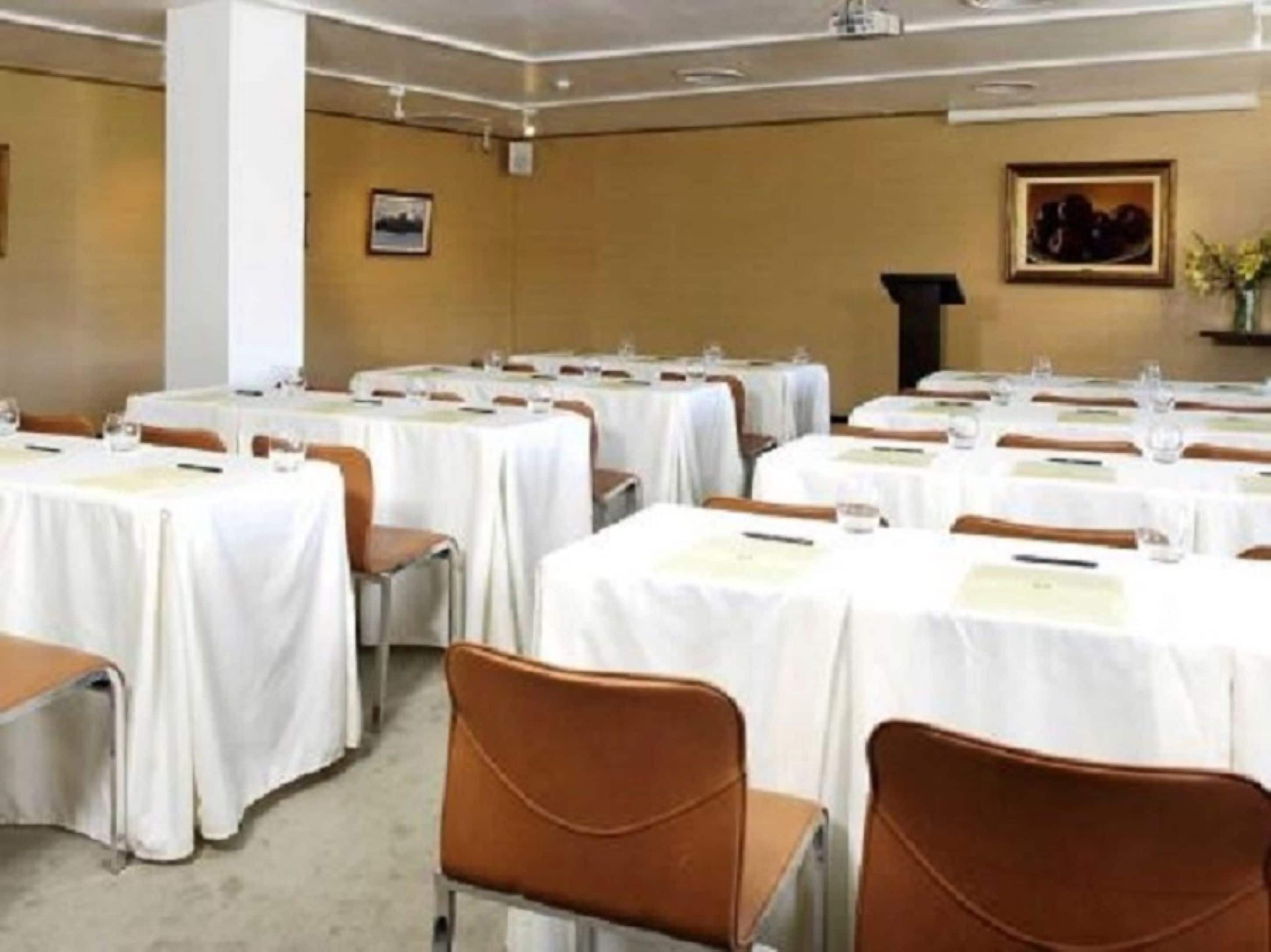 A conference room with multiple tables and chairs, arranged in rows.