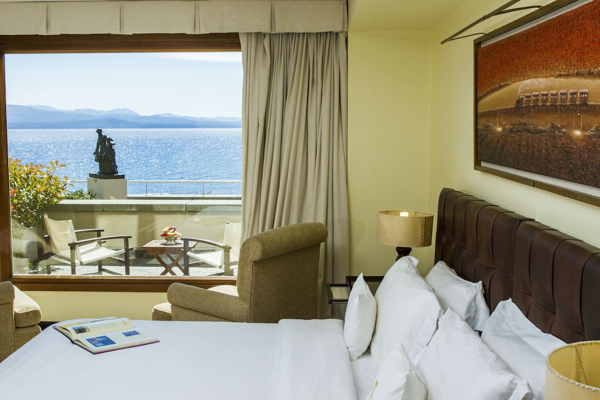 Une chambre d’hôtel avec un lit, une vue sur la mer, une statue à l’extérieur et un tableau au mur.