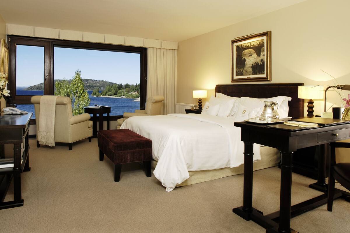 Une chambre d’hôtel avec un grand lit, un bureau, une chaise, une petite table et une vue sur la mer.