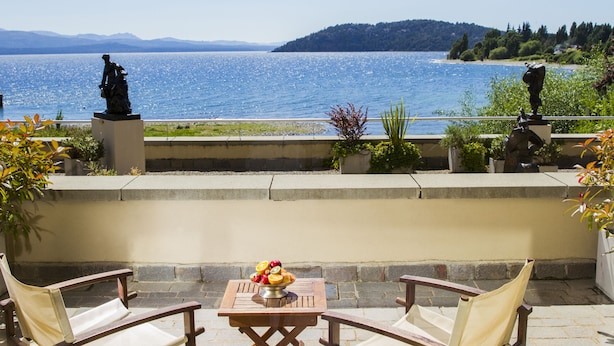 A patio with a table and chairs overlooking a lake, statues, and potted plants. - El Casco Art Hotel (San Carlos de Bariloche)