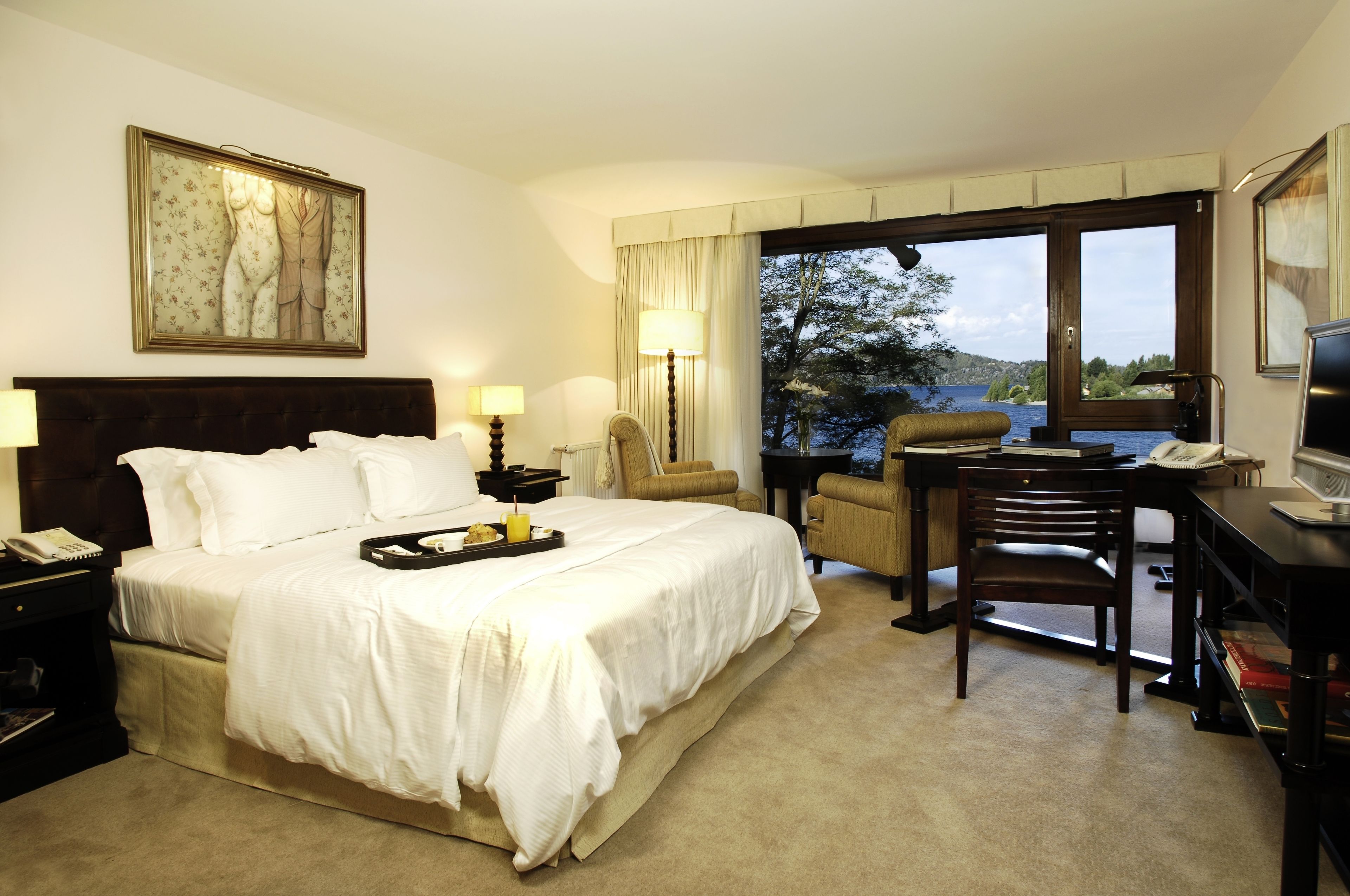 Een hotelkamer met een groot bed, een bureau, een stoel, een lamp en uitzicht op het meer.