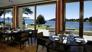 A restaurant with tables set for dining, large windows offering a view of a lake and mountains. - El Casco Art Hotel (San Carlos de Bariloche)