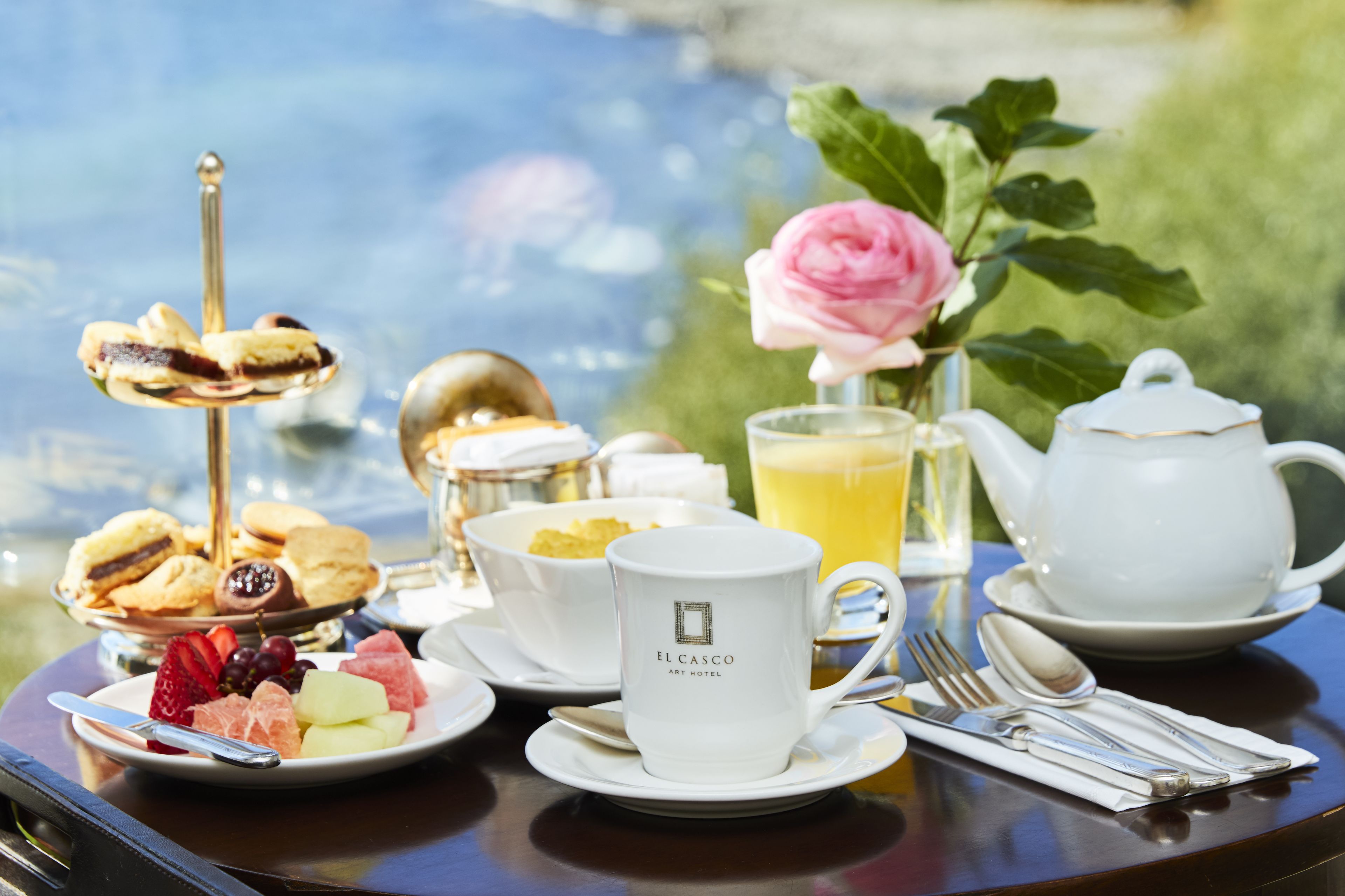 A table set with a teapot, cups, a rose, and a fruit platter.