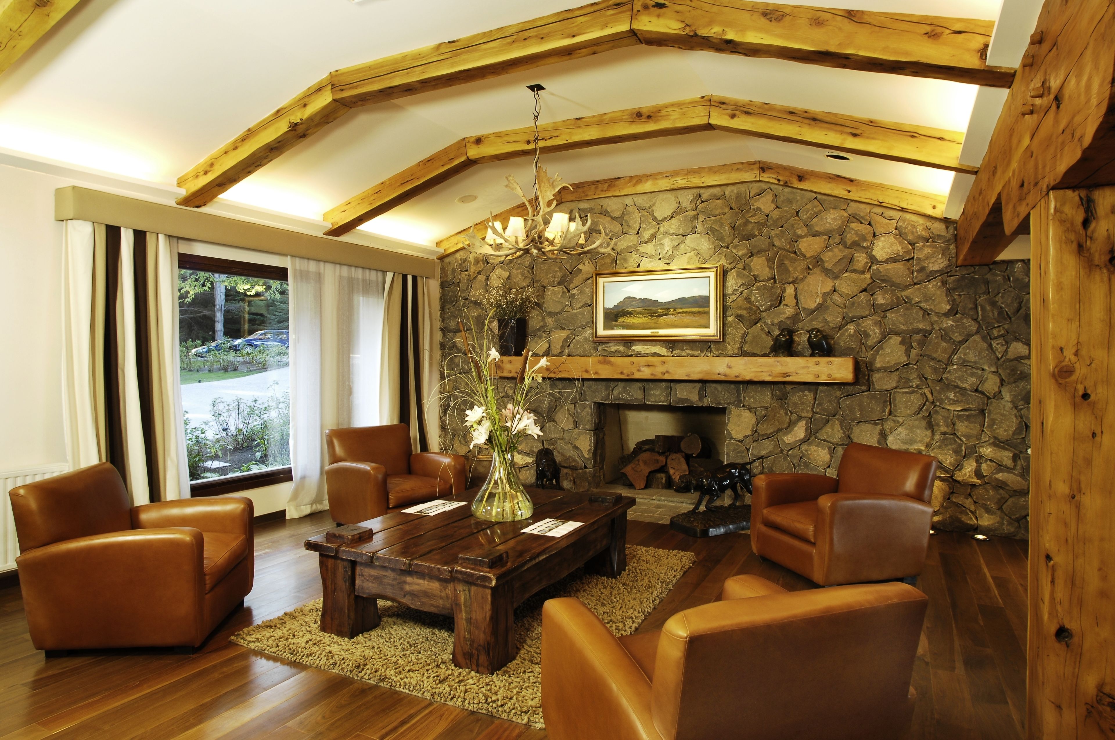 Un salon chaleureux avec des canapés en cuir, une table basse en bois, une cheminée en pierre et une grande fenêtre agrémentée de rideaux.