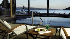 A poolside dining area with a view of a lake and mountains. There are lounge chairs and a table with a plate of food and drinks. - El Casco Art Hotel (San Carlos de Bariloche)