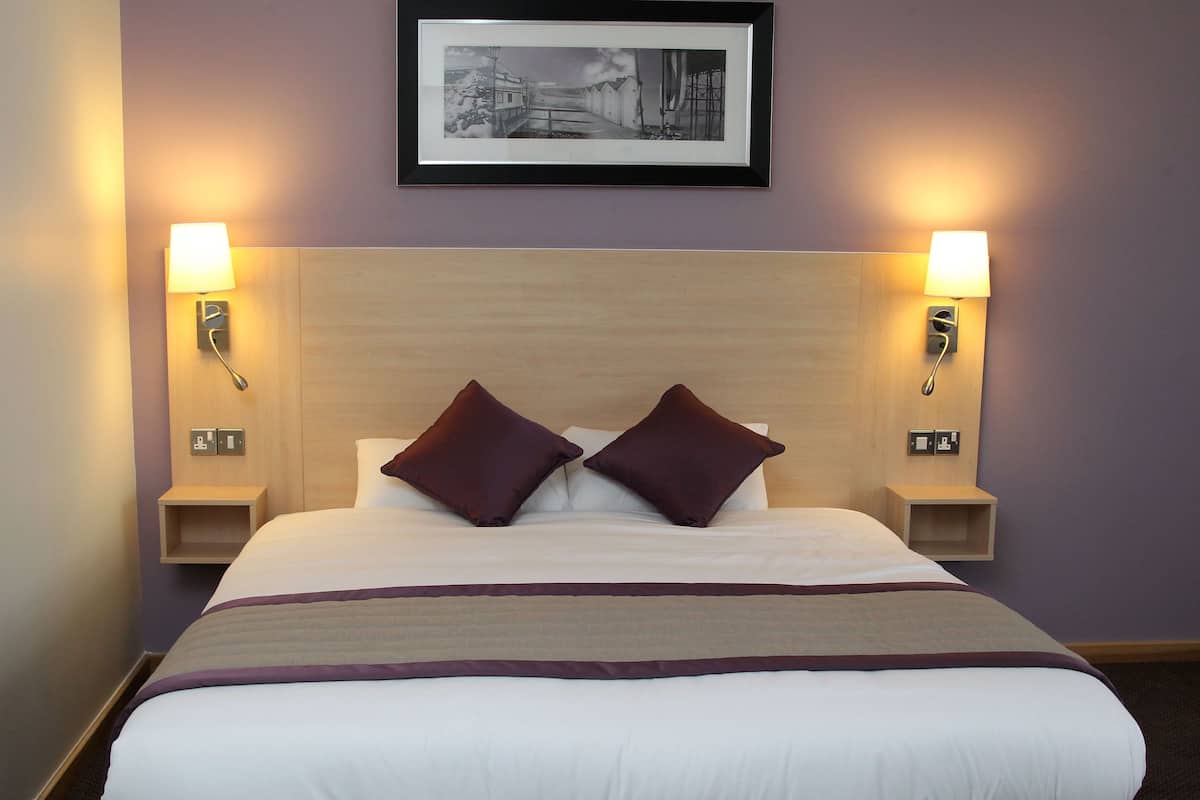 A hotel room with a large bed, two bedside lamps, and a framed picture on the wall.