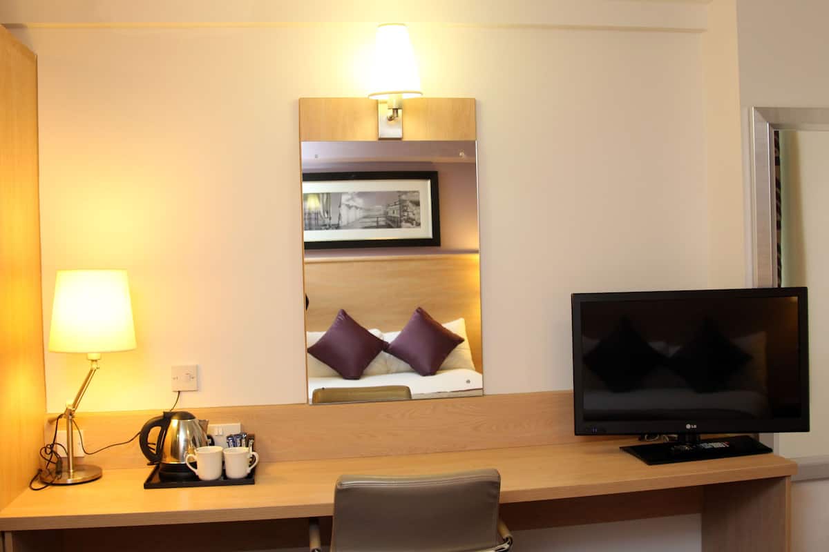 A hotel room with a wooden desk, a television, a lamp, a coffee maker, and a framed picture on the wall.