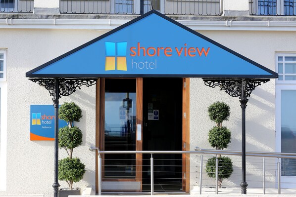 A hotel entrance with a blue awning, a signboard, and a glass door. - Shore View Hotel (Eastbourne)