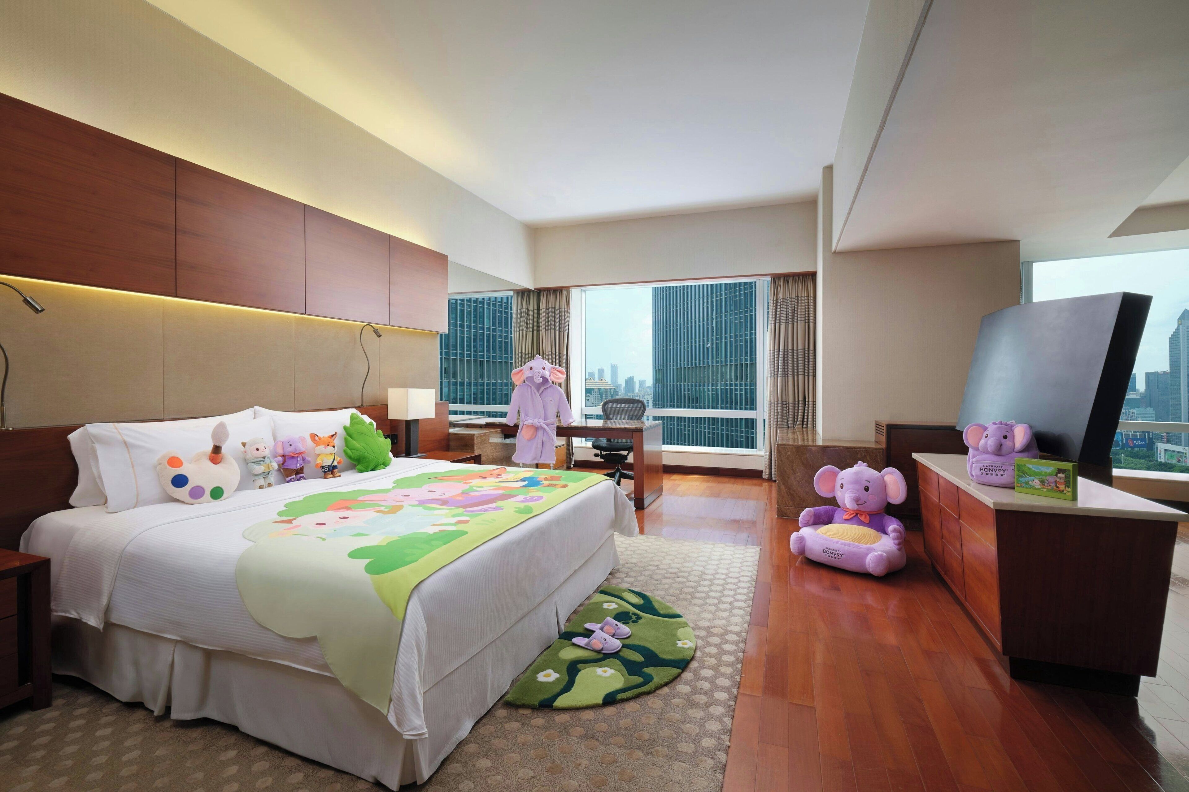 A hotel room with a large bed, a desk, a TV, and a view of the city.