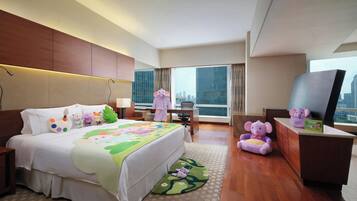 A hotel room with a large bed, a desk, a TV, and a view of the city.