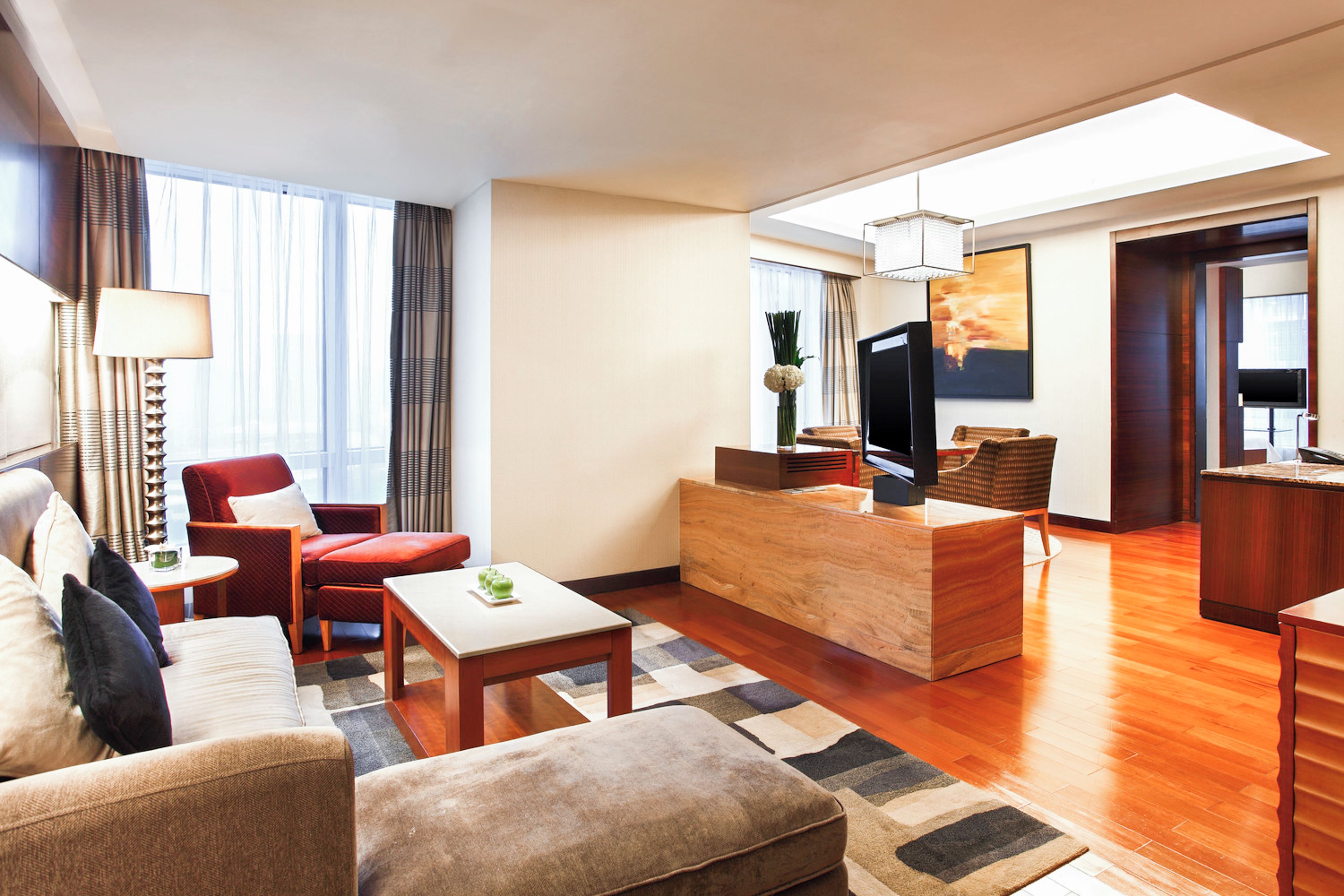 Una habitación de hotel moderna con sofá, sillón, mesa de centro y zona de televisión con televisor de pantalla plana y una mesita de madera.