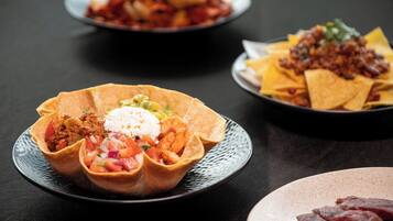 Three plates of food, including tacos and nachos, on a dark table.