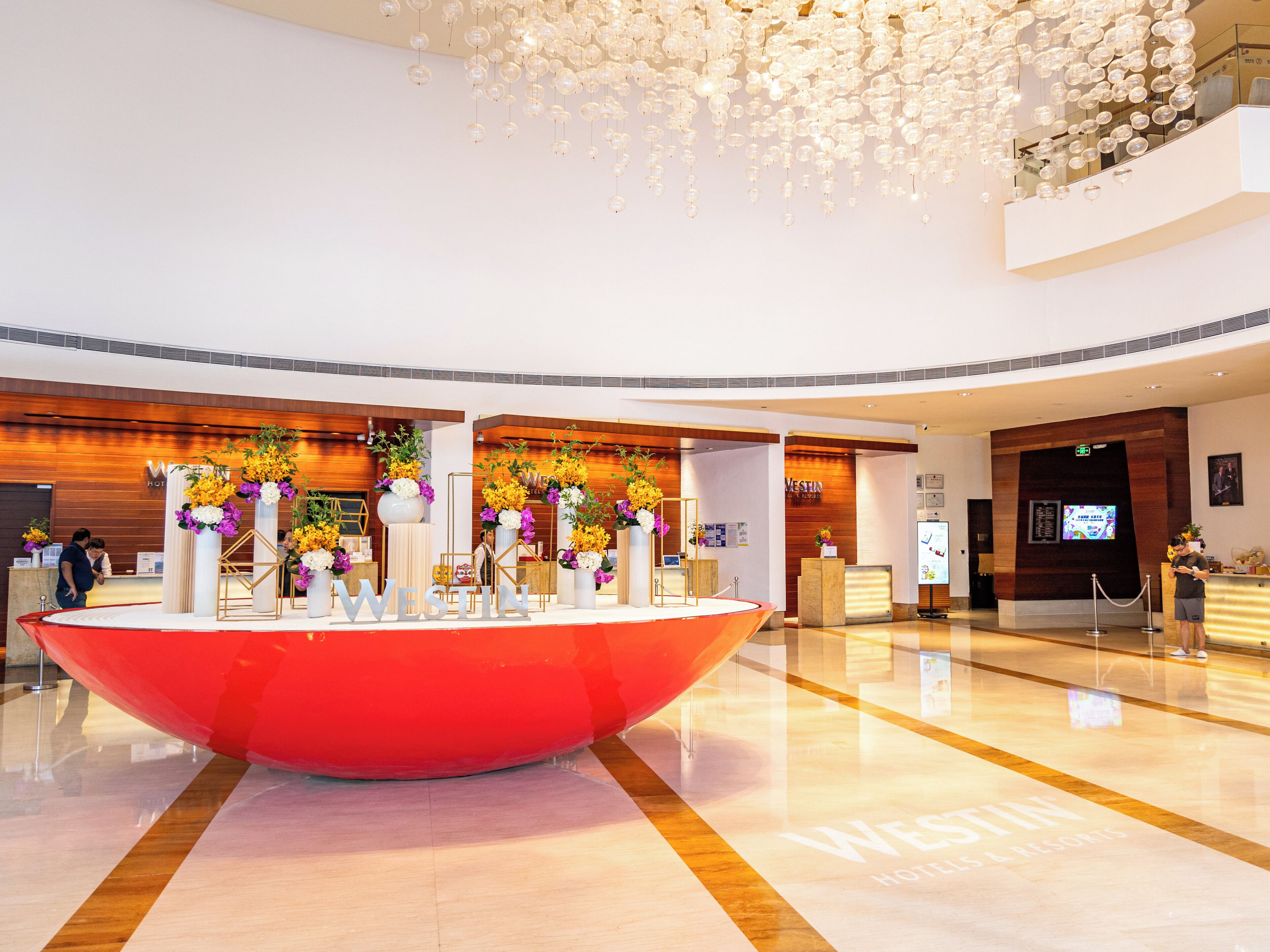 A modern hotel lobby with a large red centerpiece, wooden accents, and a chandelier.